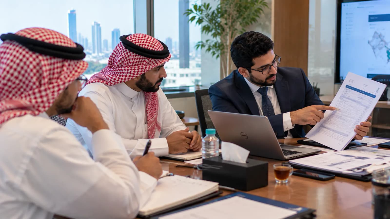 مستشار يرفع مستند ترخيص ويشير إلى أحد بنوده لعميلين على الجانب الآخر من الطاولة.