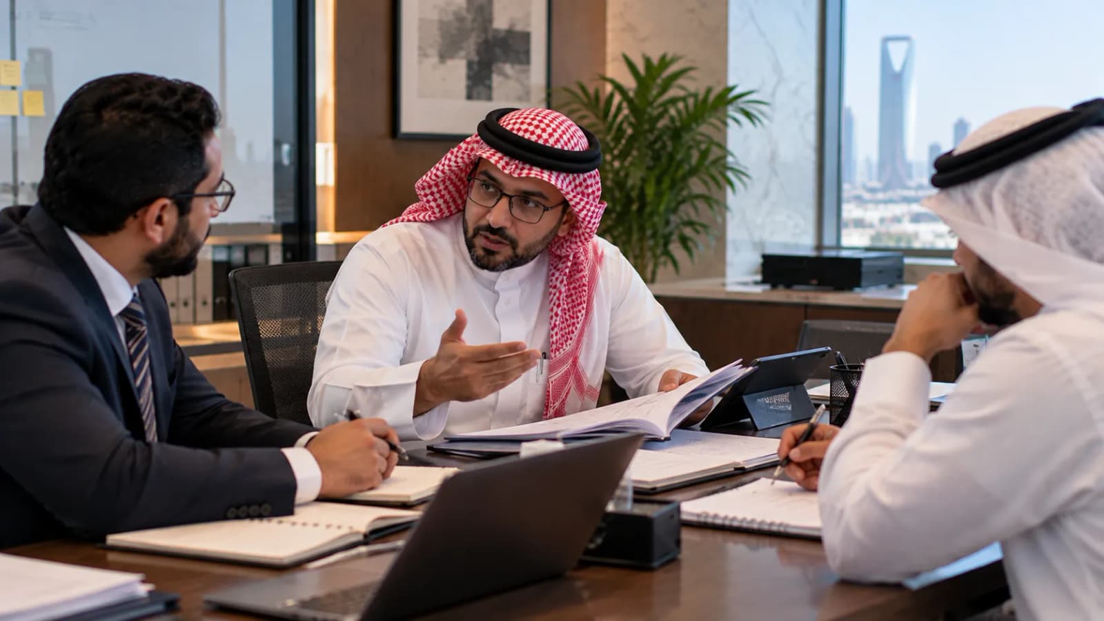 مستشار يشرح ملف موظفين مفتوحًا لزميلين يدوّنان ملاحظاتهما على طاولة اجتماعات